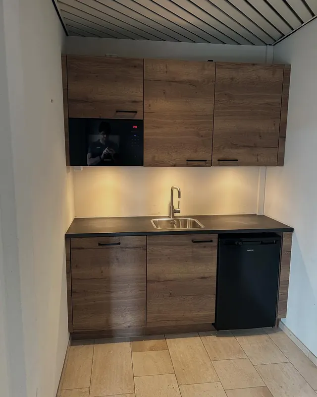 Compacte keuken met houtlook kasten, donker werkblad en ingebouwde oven.