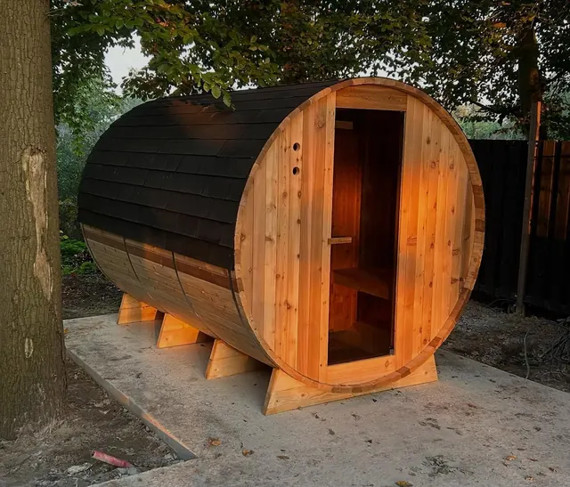 Houten barrelsauna in een groene tuin.