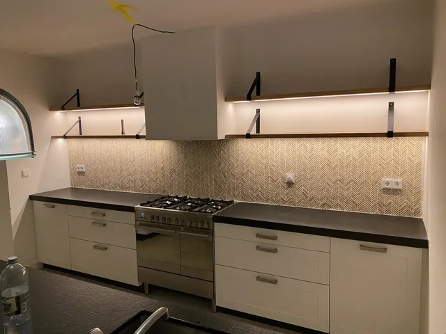 Afgewerkte keuken met houten planken aan de vernieuwde achterwand.