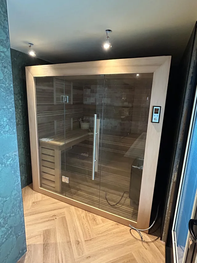 Afgewerkte sauna met houten binnenbekleding, banken en een glazen deur.