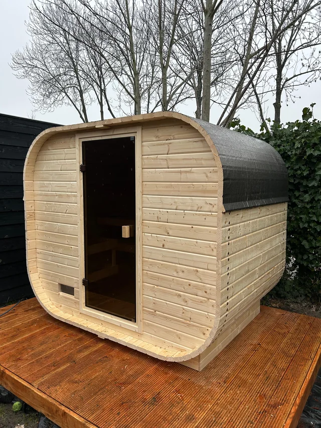 Lichte houten barrelsauna op een houten terras in de tuin.