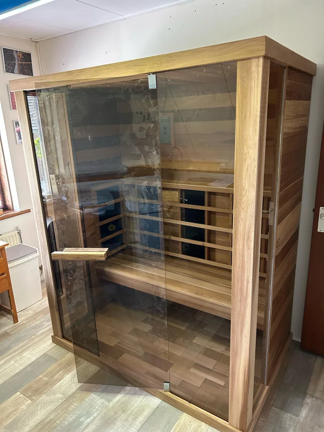 Saunacabine van licht hout met glazen voorzijde en houten banken.